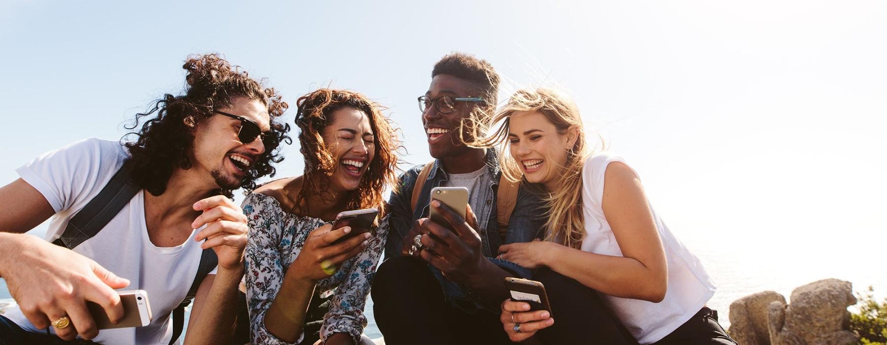 a group of friends sit outside laughing over their cell phones